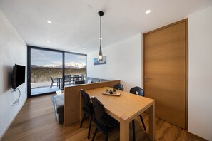 A modern dining area with a wooden table, black chairs, and a view of mountains through large windows.