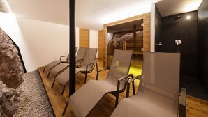 Habitación con piso de madera, pared de piedra y pared negra con ducha. Hay cuatro sillas con respaldo de malla.