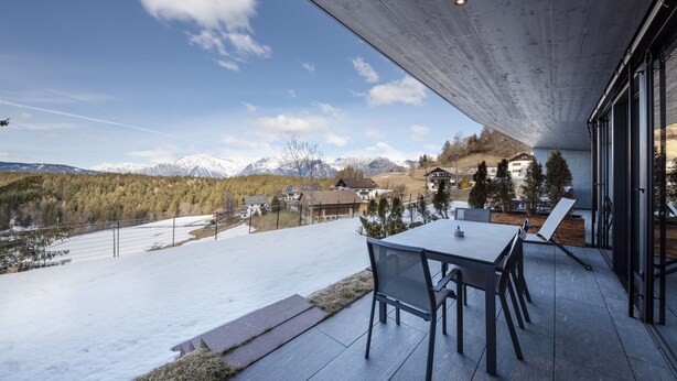Un patio exterior moderno con una mesa y sillas, con vistas a un paisaje nevado y montañas.