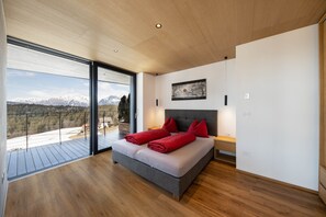 A modern bedroom with a large bed, a view of mountains, and a balcony.