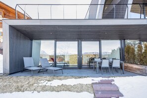 Eine moderne Außenpatio mit Sitzgelegenheiten, einem Essbereich und großen Glasfenstern.