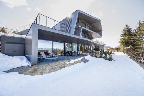 A modern multi-story building with a balcony, large windows, and a snowy landscape.