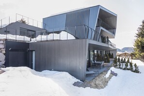 Ein modernes, zweistöckiges Gebäude mit Balkon, Steinwand und verschneiter Landschaft.