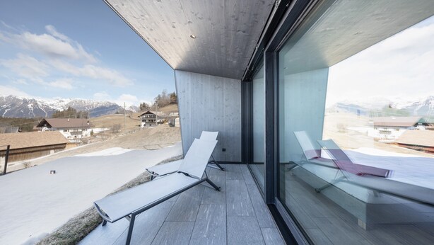 Ein Balkon mit Blick auf schneebedeckte Berge, moderne Architektur und eine Glasabtrennung.