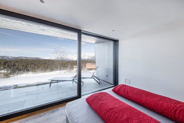 A modern bedroom with a large window, a bed with red pillows, and a view of a snowy landscape. - Apartment 'Hirzer Residenze Moritz' Close to Merano with Mountain View & Garden (Avelengo)