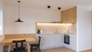 Une cuisine moderne avec une table à manger en bois, deux chaises, un luminaire suspendu et des appareils électroménagers intégrés.