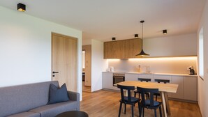 Una cocina moderna con armarios de madera, un comedor con mesa y sillas, y un sofá gris con un cojín.