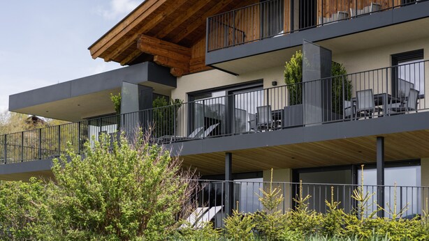 Un edificio de varios pisos con balcones, mobiliario exterior y fachada de madera.