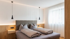 Un dormitorio moderno con una cama grande, dos mesitas de noche y una ventana con cortinas de gasa.