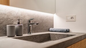 Un baño con un lavamanos moderno, dos dispensadores de jabón y una toalla.