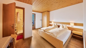 A bedroom with a wooden ceiling, two beds, a wooden nightstand, and a door leading to a bathroom. - Holiday Apartment "Grödnerhof - Almöhi" Mountain View, Wi-Fi, Garden & Balcony (Breien / Tiers)