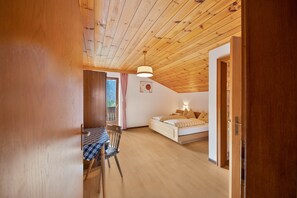Une pièce avec un plafond en bois, un lit avec des oreillers, une table avec une chaise et une fenêtre avec des rideaux.