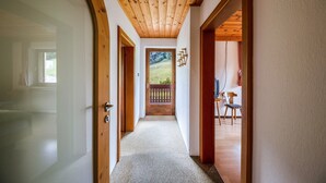 A hallway with wooden ceilings and doors leading to a balcony with a view of a grassy landscape.