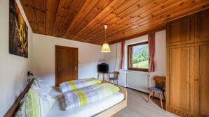 A bedroom with a bed, wooden ceiling, a television, a window with curtains, and a radiator.