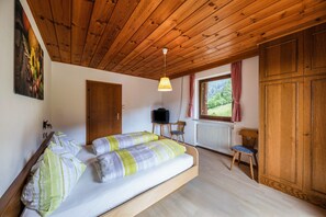 A bedroom with a bed, wooden ceiling, a television, a window with curtains, and a radiator.