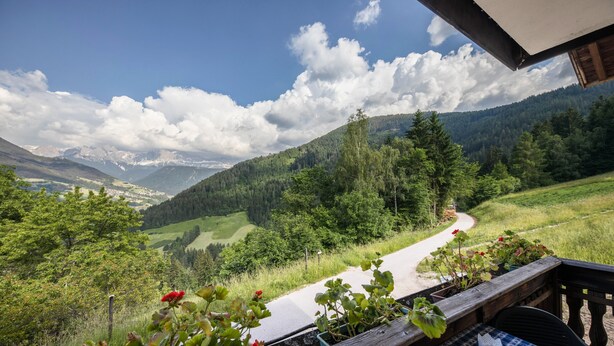 A balcony with a view of a winding road, lush greenery, and distant mountains.