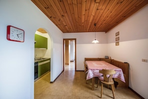 A dining area with a table and chairs, a clock on the wall, and a kitchen visible through an archway.