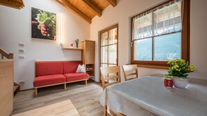 A room with a wooden ceiling, a red sofa, a dining table with a white tablecloth, and a window with a view. - Apartment "Kreuzhof rechts" with Mountain View, Wi-Fi, Balcony & Garden (Neustift)