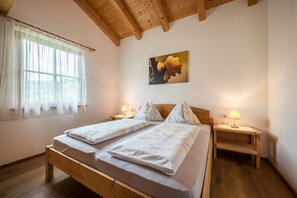 A room with a wooden bed, two bedside tables with lamps, a window with sheer curtains, and a painting on the wall.