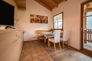 A kitchen with a television, a dining table with chairs, a painting on the wall, and a window with a view.