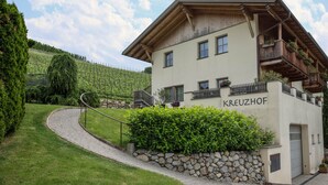 A building with a stone wall, a curved pathway, and a wooden balcony with flowers. - Apartment "Kreuzhof links" with Mountain View, Wi-Fi, Balcony & Garden (Neustift)