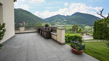 Eine Terrasse mit Gartenmöbeln, einem Blumentopf und Blick auf Berge und ein Tal.