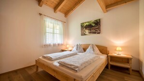 A wooden bed with two pillows and a nightstand with a lamp. - Apartment "Kreuzhof links" with Mountain View, Wi-Fi, Balcony & Garden (Neustift)