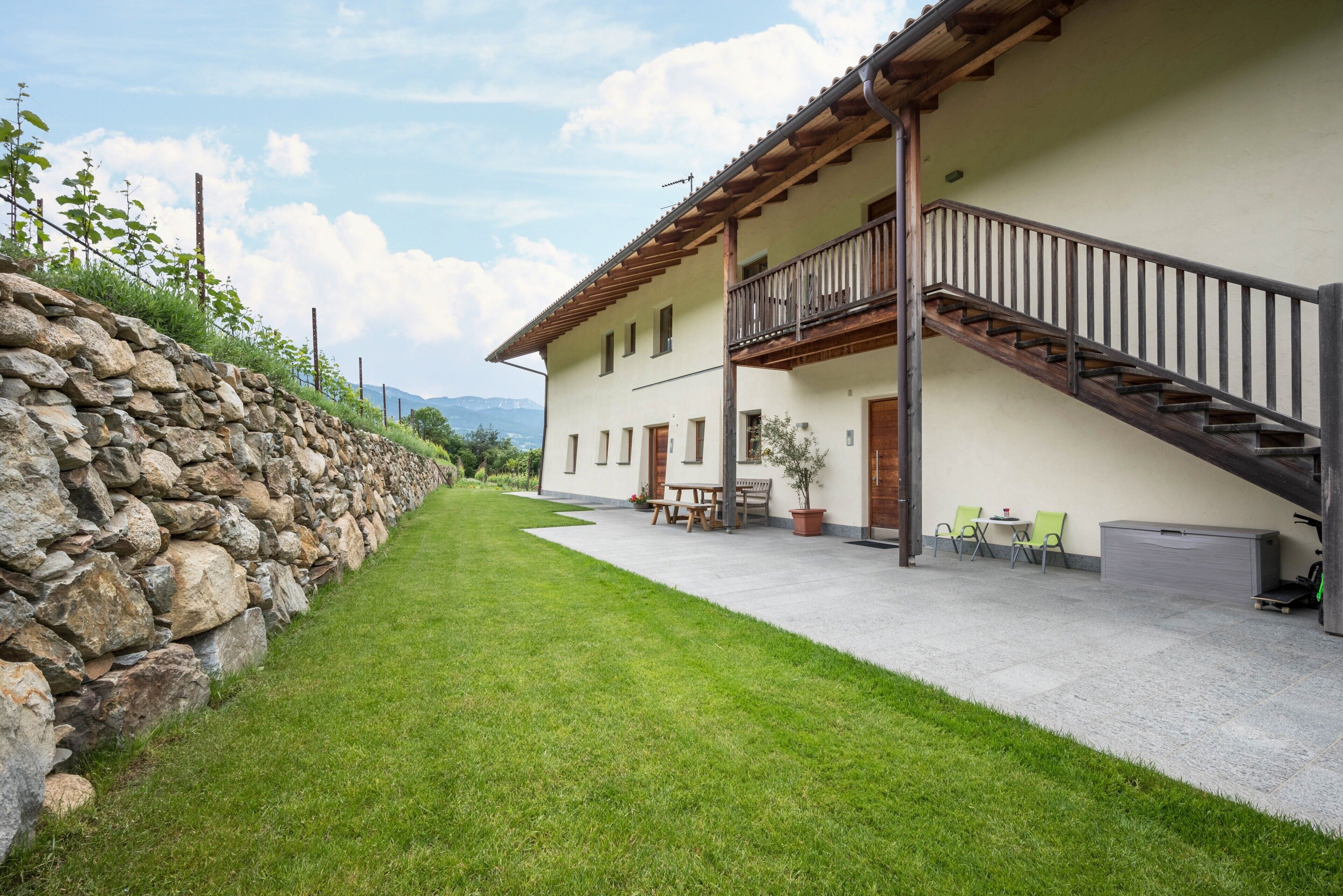 A two-story building with a stone wall, a balcony, and a staircase.