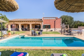 Una piscina con lettini, una zona patio e un edificio con tetto in tegole.