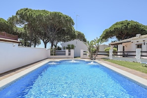 A rectangular swimming pool with a tiled edge, surrounded by a low white wall and a grassy area with trees.