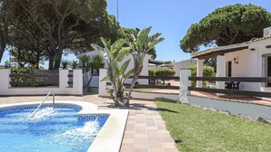 Ein Pool mit einer gefliesten Kante, umgeben von einem gepflasterten Weg, neben einem Gebäude mit weißer Fassade und einer überdachten Terrasse.