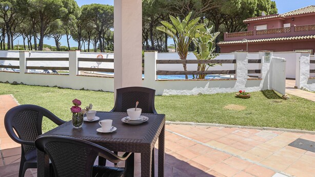 Eine Terrasse mit Tisch und Stühlen, einer kleinen Pflanze und Blick auf Pool und Bäume.