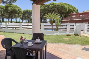 A patio with a table and chairs, a small plant, and a view of a pool and trees.