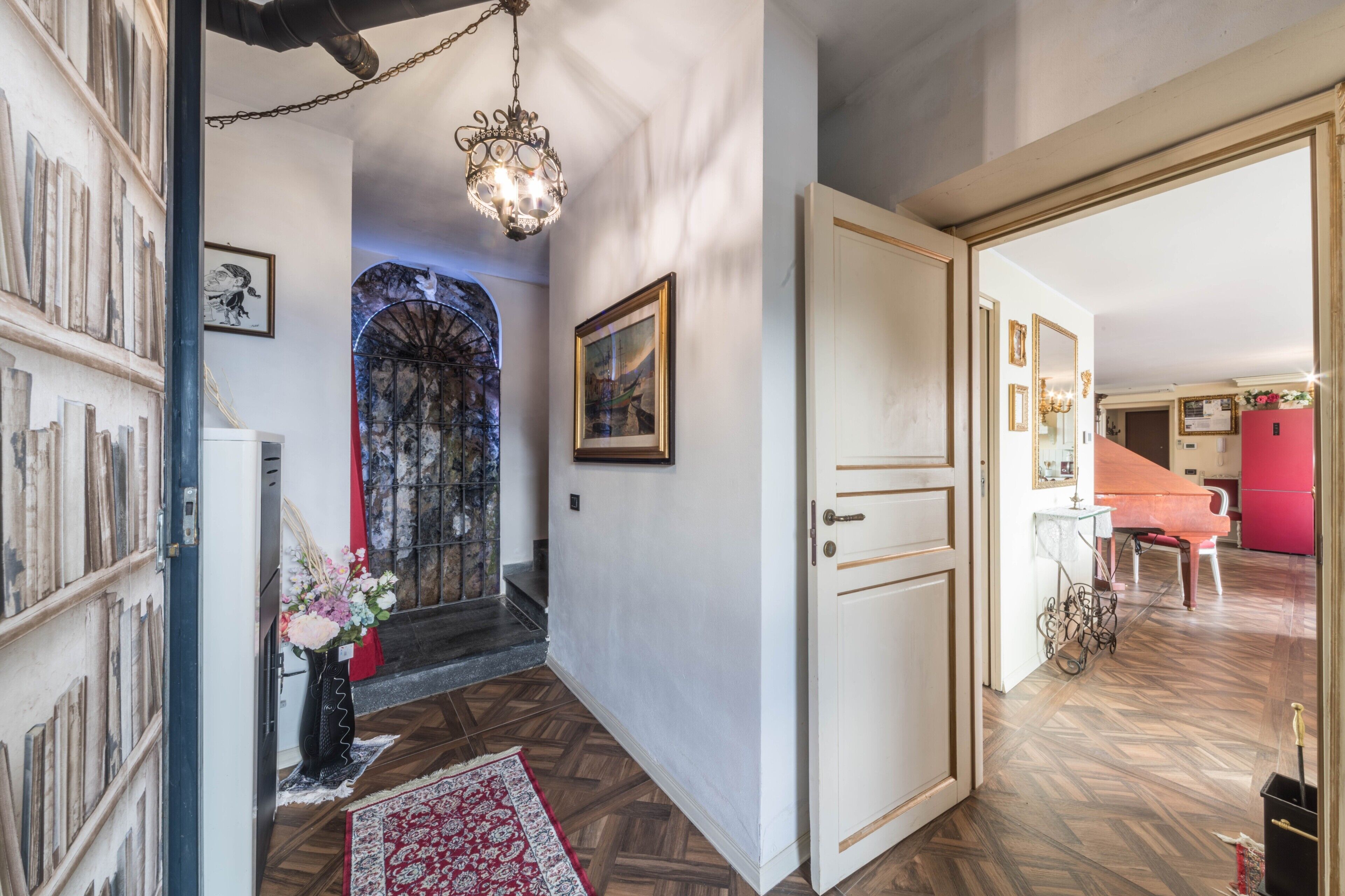 Um corredor com piso de madeira, um lustre, uma porta e um tapete vermelho.