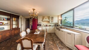 Ein Esszimmer mit Holztisch und Stühlen, einem Kronleuchter und Blick auf Berge durch ein großes Fenster.