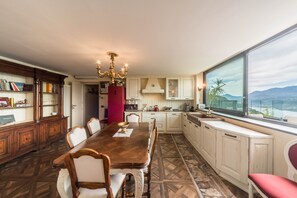 Une salle à manger avec une table et des chaises en bois, un lustre et une vue sur les montagnes par une grande fenêtre.