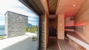Eine moderne Sauna mit Holzwänden und einer Steinfassade, ein Holzboden sowie Bergblick.