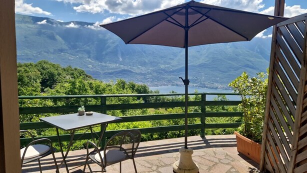 Eine Terrasse mit Tisch und Stühlen, einem großen Sonnenschirm und Blick auf Berge und einen See.