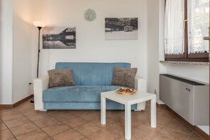 Un soggiorno con un divano blu, un tavolo bianco, una lampada da terra e un termosifone.