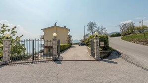 Ein verschlossenes Tor mit einem Gebäude, einer gepflasterten Auffahrt und einer sich im Hintergrund windenden Straße.