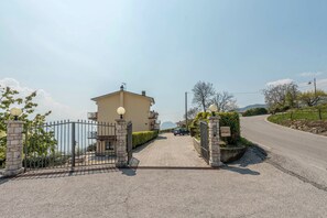 A gated entrance with a building, a paved driveway, and a road curving in the background.