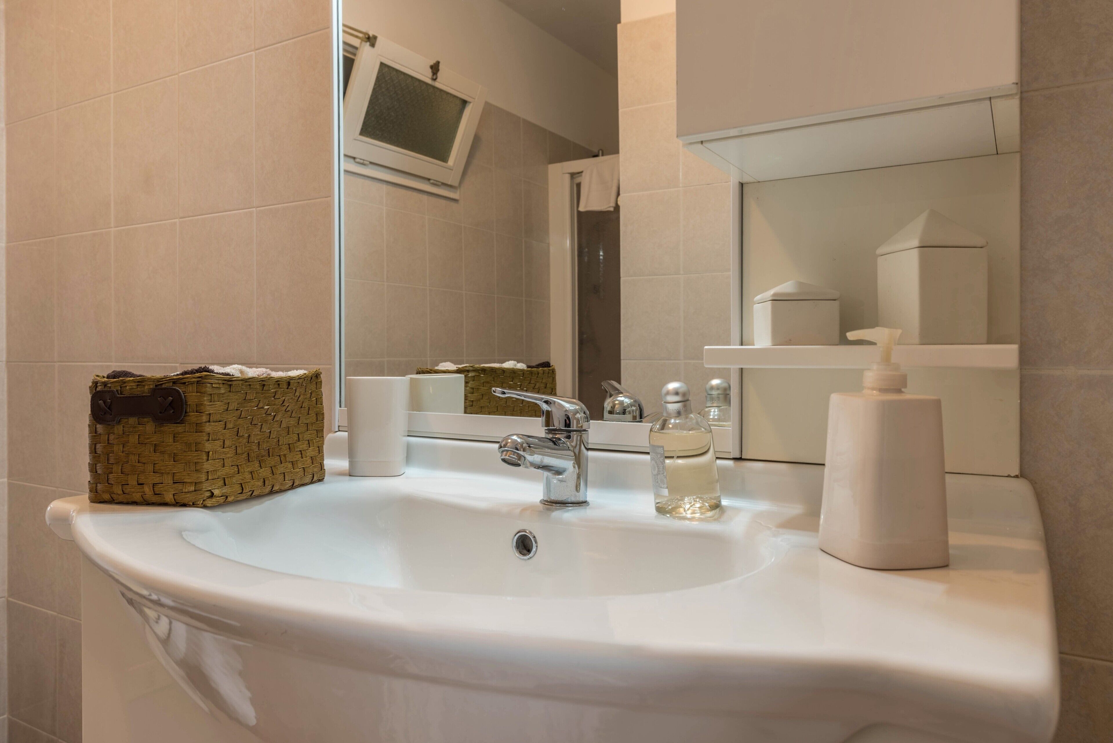 A bathroom with a white sink, a mirror, a television mounted above the mirror, and a small shelf with toiletries.
