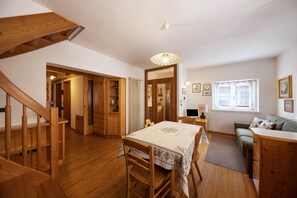 Un escalier en bois mène à un espace repas comprenant une table et des chaises, un canapé et une fenêtre avec des rideaux.