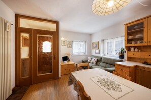 Une pièce avec une porte en bois, un bureau avec un ordinateur, un canapé et une table à manger recouverte d’une nappe.