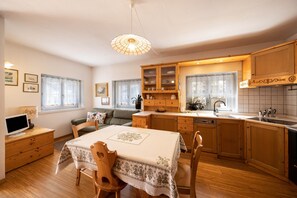 Une cuisine de taille réduite avec des meubles en bois, une table à manger avec des chaises, un four encastré et une fenêtre avec des rideaux.