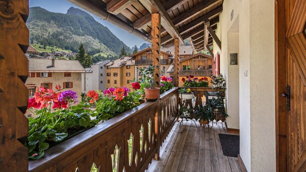 Ein Holzbalkon mit Blumentöpfen, einem Holengeländer und Blick auf einen Berg.