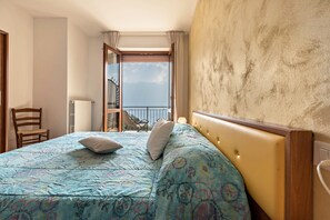 A hotel room with a bed, a chair, a window with a view, and a balcony.