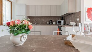 A modern kitchen with marble countertops, a coffee machine, and a vase with flowers on the table.