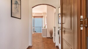 A hallway with a wooden door, a framed picture on the wall, and a view to a balcony with a railing.