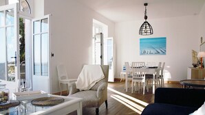 Un salon spacieux comprenant un coin repas, un canapé, un fauteuil avec une couverture et un tableau accroché au mur.